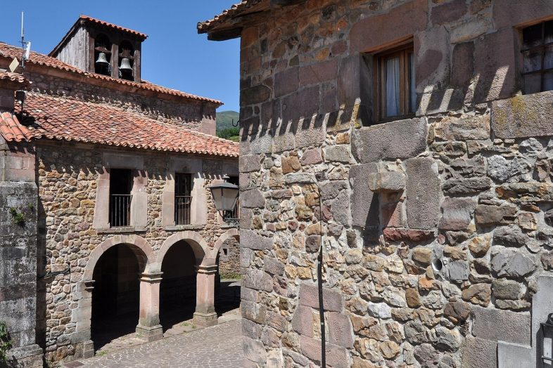 Casona montañesa con soportal de arcos de piedra en Carmona, con la espadaña de la iglesia detrás