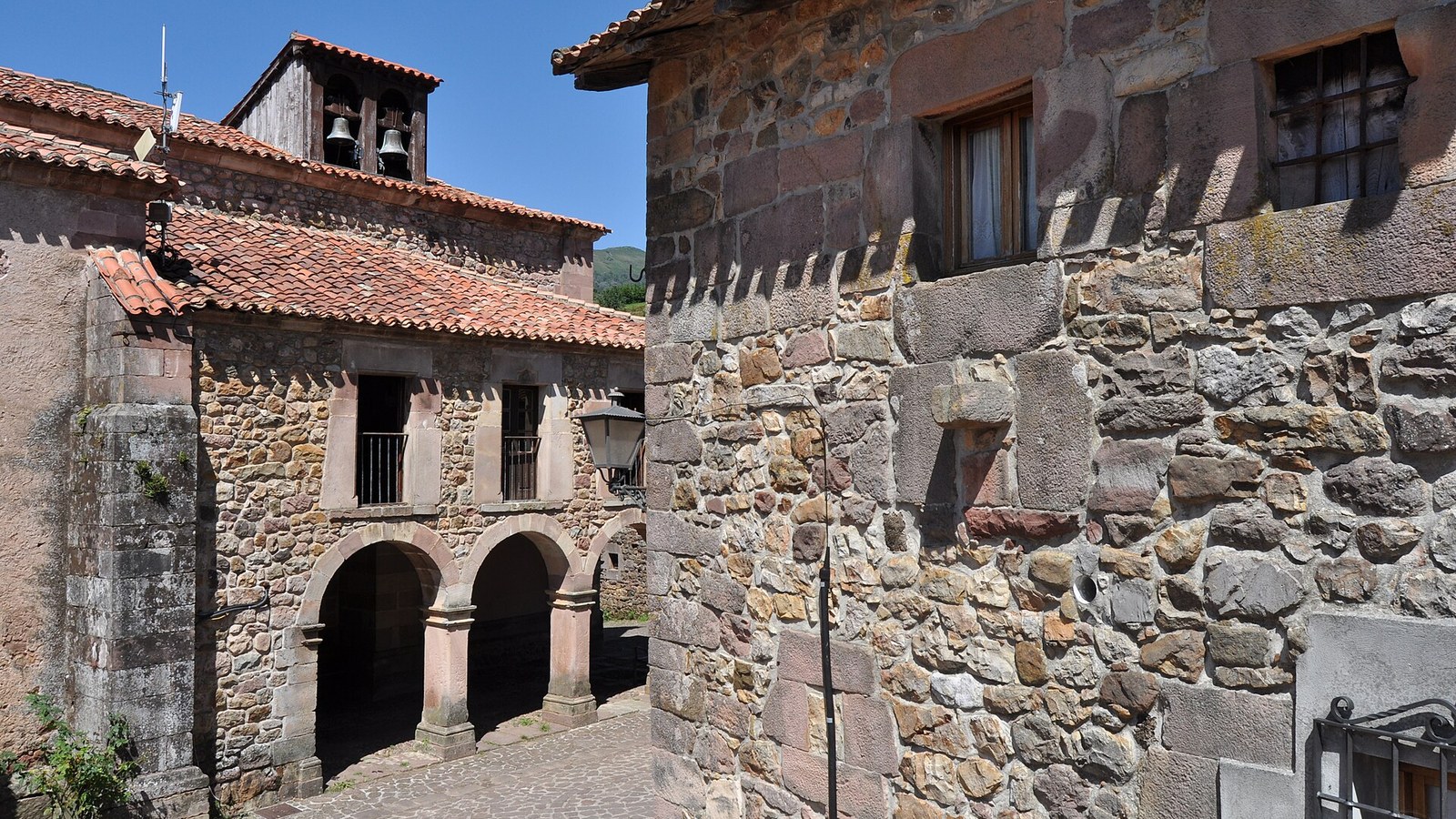 Casona montañesa con soportal de arcos de piedra en Carmona, con la espadaña de la iglesia detrás