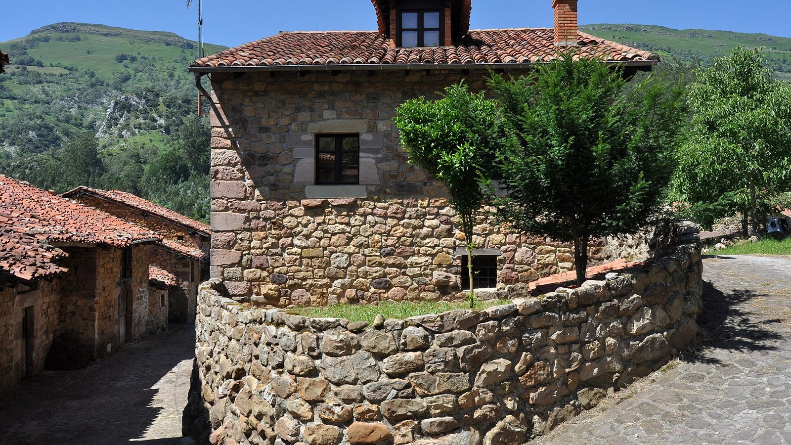 Casona de piedra de Carmona con los prados y los montes del valle de Cabuérniga detrás
