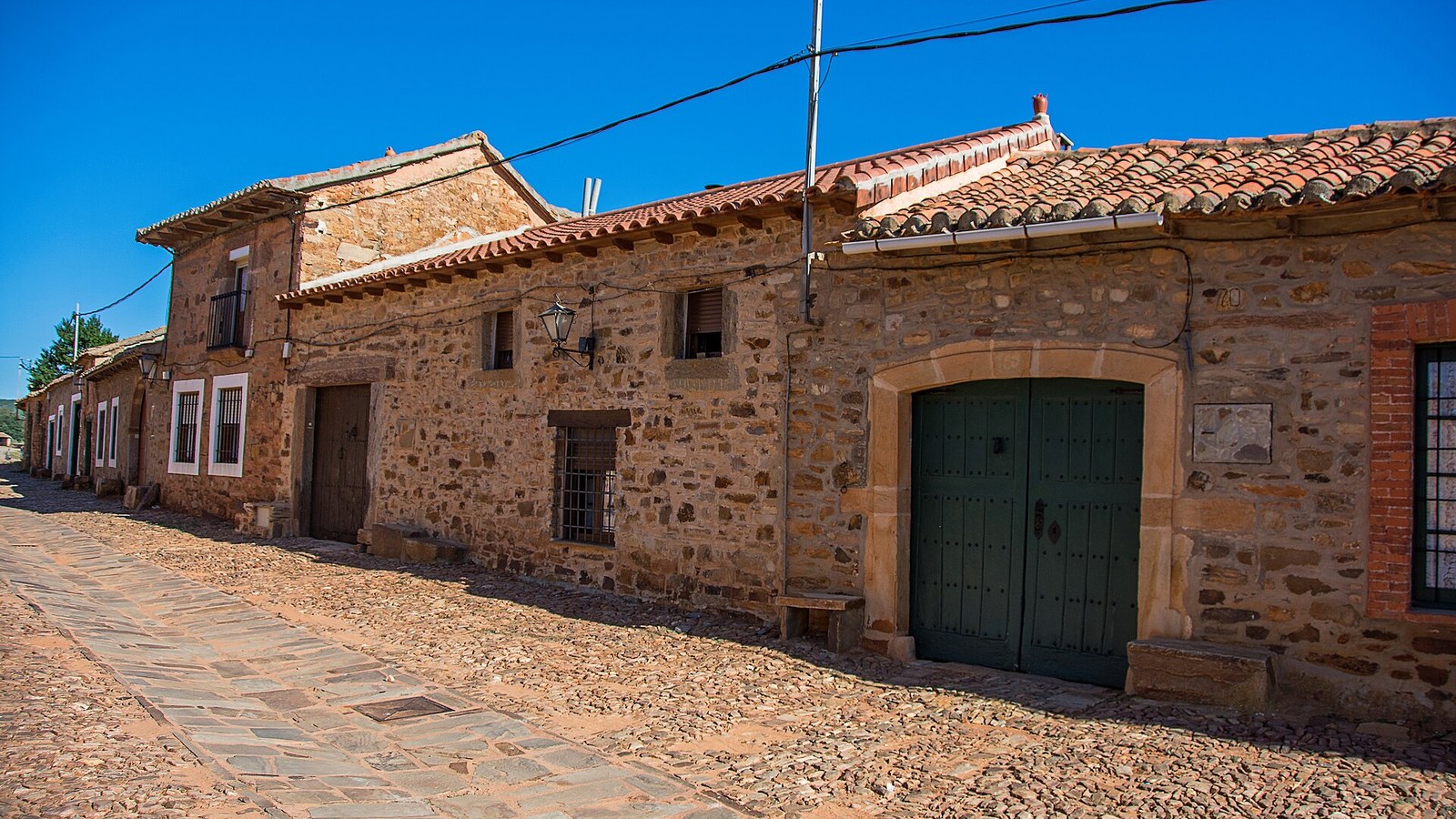 Calle empedrada de Castrillo de los Polvazares con las casas de piedra rojiza y las puertas verdes