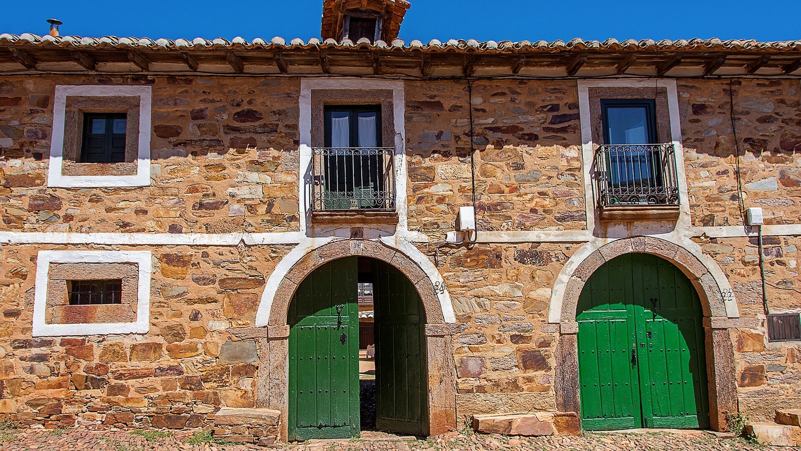 Fachada de una casa arriera maragata con dos grandes portones verdes para el paso de carros
