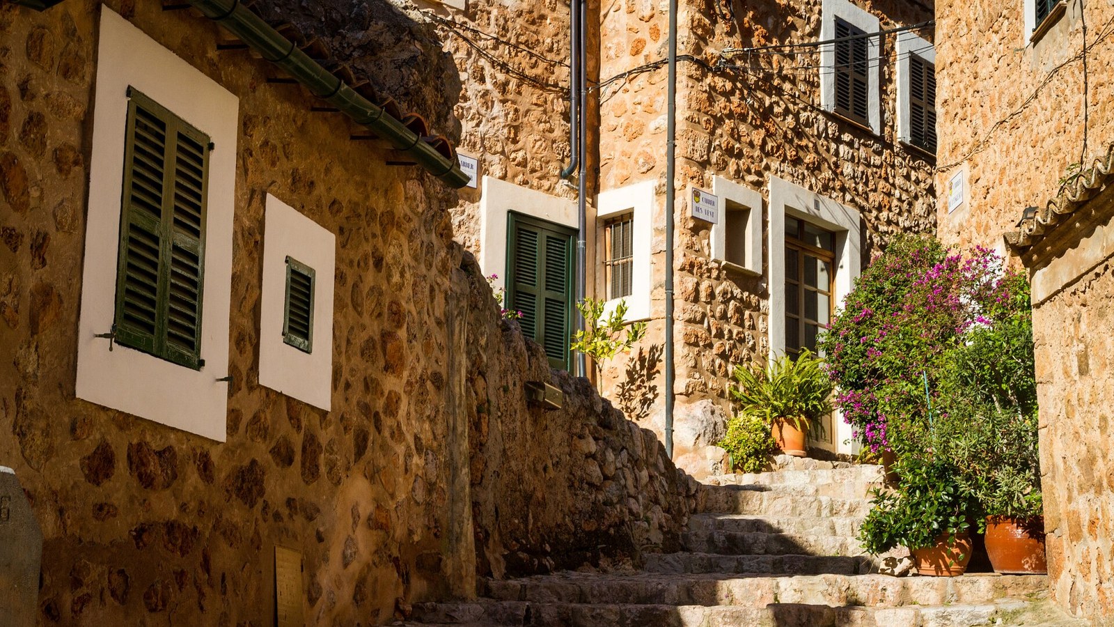 Calle empedrada con escalones y macetas entre casas de piedra de Fornalutx