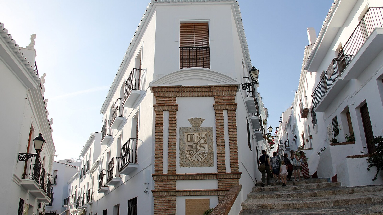 Calle empinada y encalada del barrio mudéjar de Frigiliana con el escudo de la villa