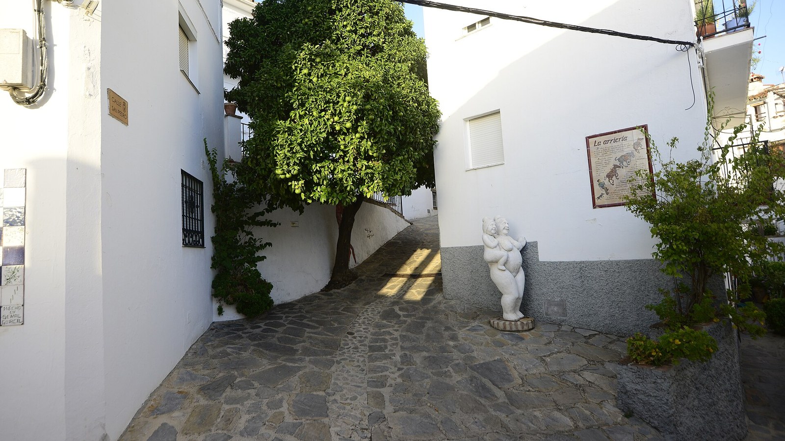 Calle empedrada de Genalguacil con una escultura blanca junto a una casa encalada