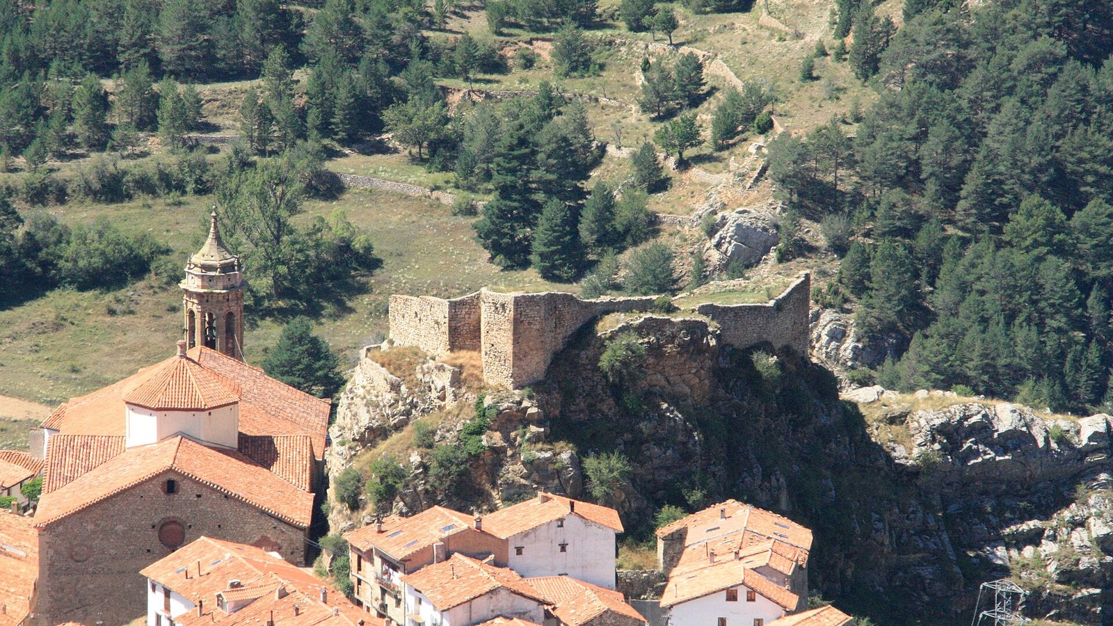 Los restos del castillo de Linares de Mora sobre los tejados y el campanario exento