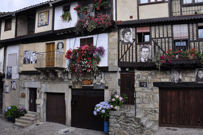 Fachada de Mogarraz cubierta de retratos pintados de vecinos, entre balcones de madera y flores