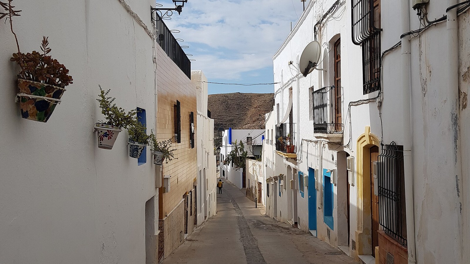 Calle encalada de Níjar con macetas colgadas en las fachadas y la sierra al fondo