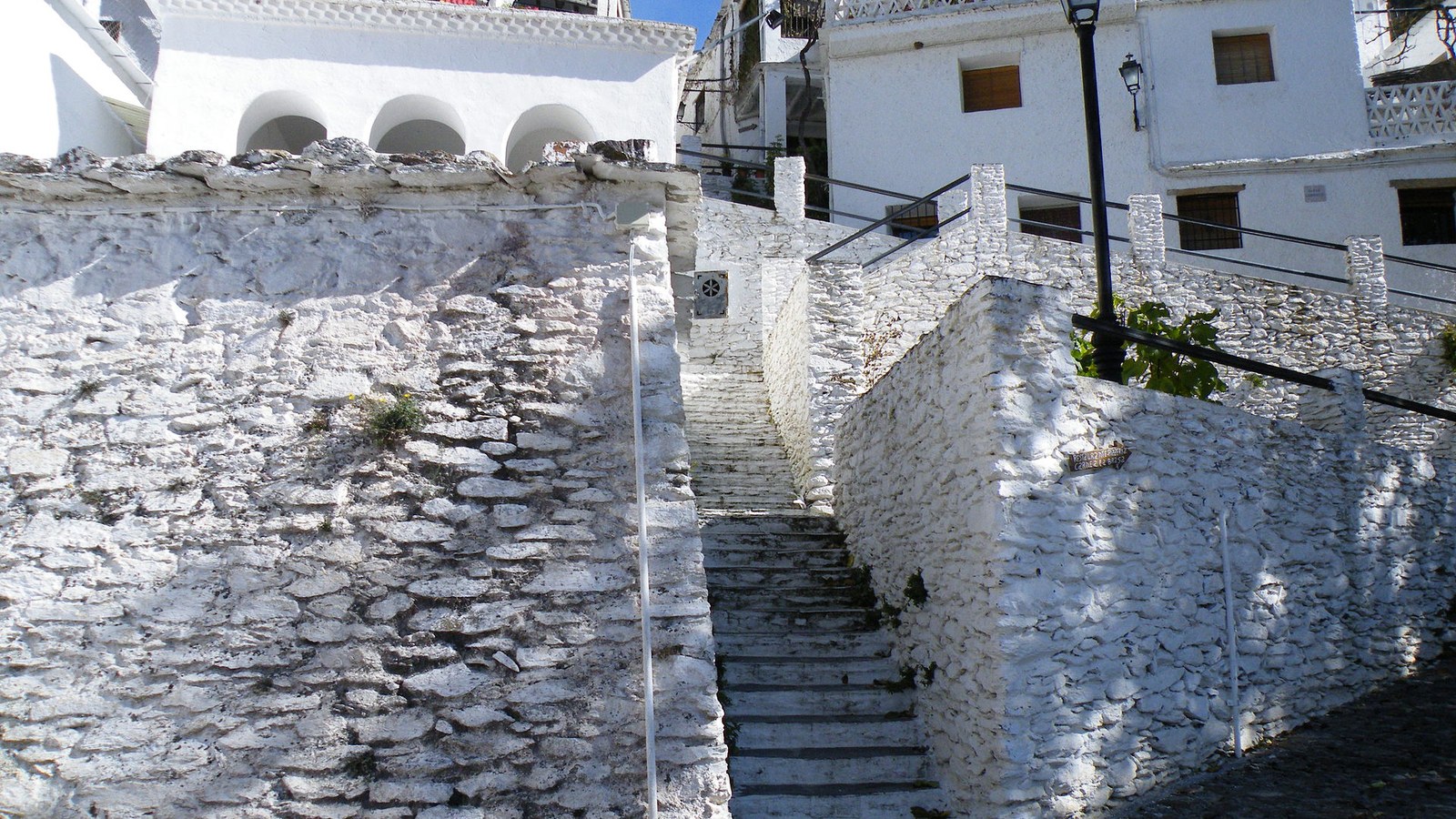 Calle en cuesta con escalones y muros de piedra encalada en Pampaneira
