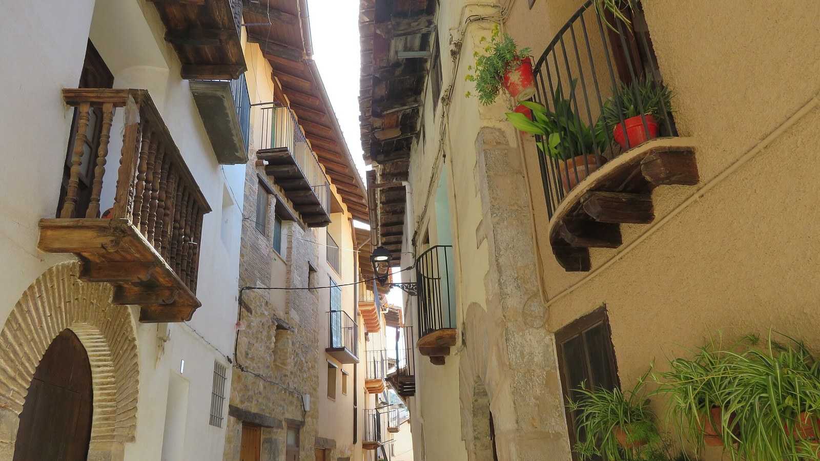 Calle de Peñarroya de Tastavins con balcones de madera, macetas y un arco de piedra