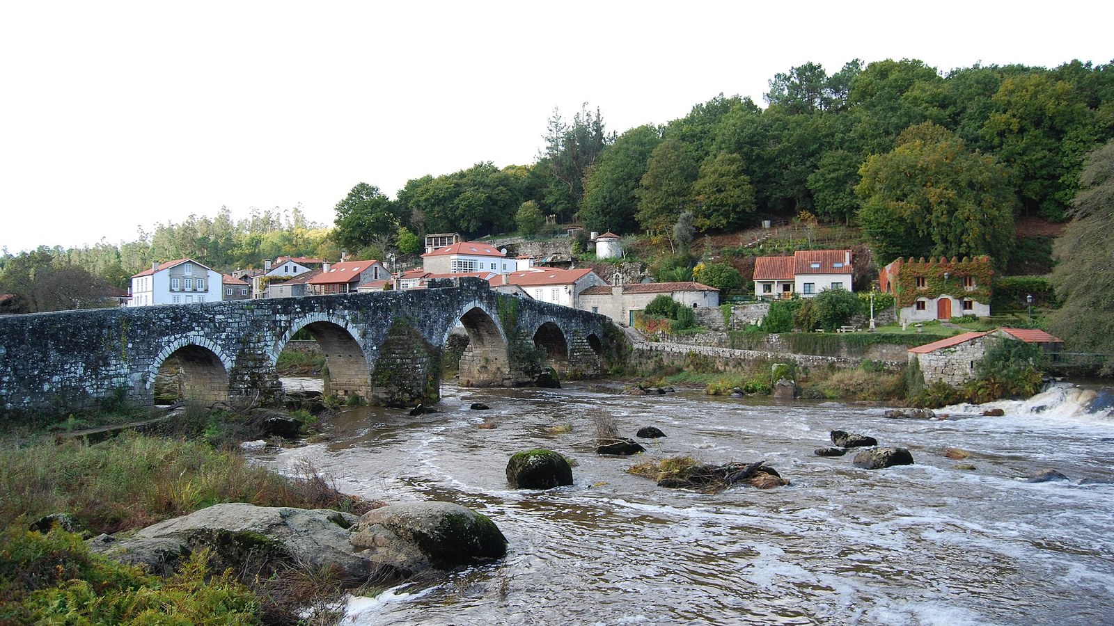 El puente medieval de Ponte Maceira sobre el río Tambre, con las casas del lugar detrás