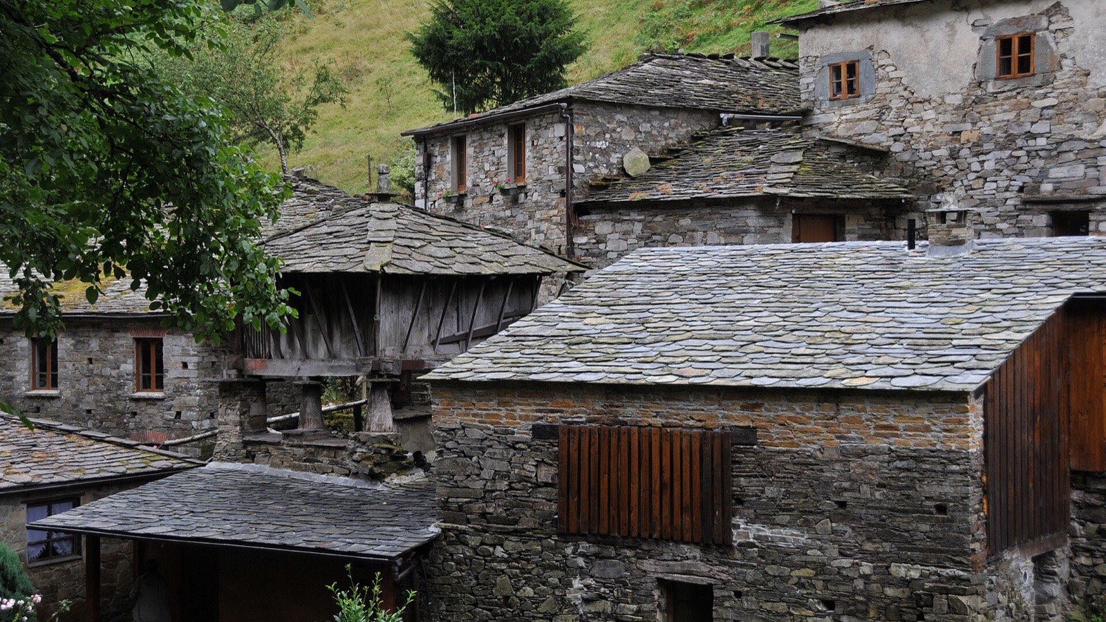 Casas y hórreo de pizarra con tejados de losa en una ladera verde de Taramundi