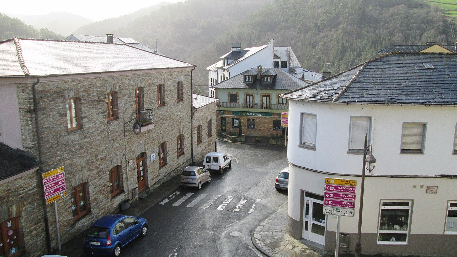 Calle de Taramundi con casas de piedra, tejados de pizarra y señales hacia Mazonovo, Esquíos y Teixois