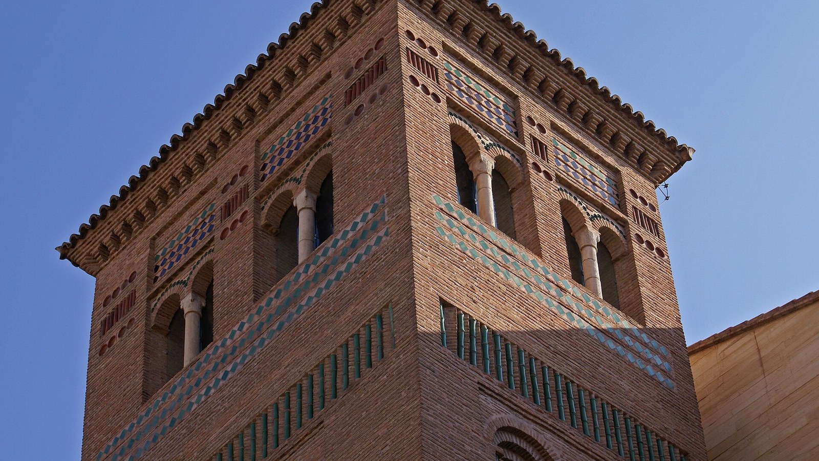 Torre mudéjar de ladrillo con cerámica vidriada verde y blanca sobre cielo azul