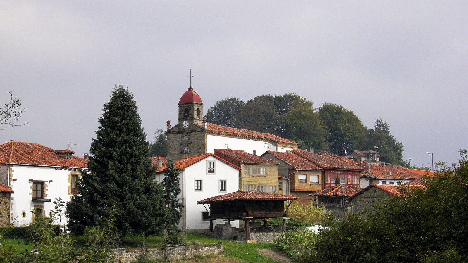 Torazo con su iglesia, las casas blancas y un hórreo entre los prados de Cabranes