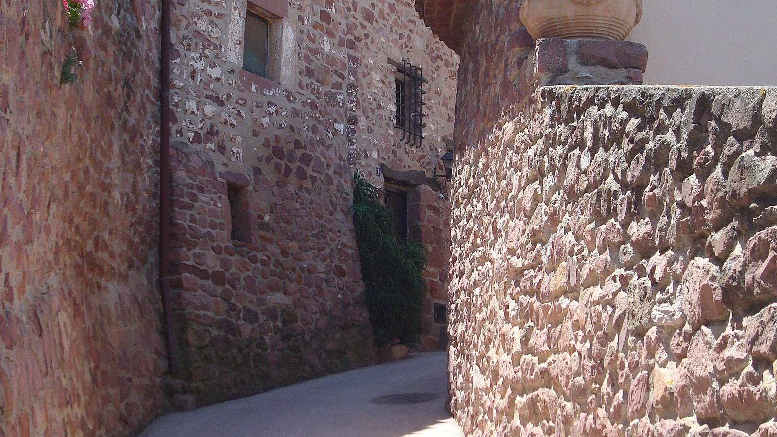 Calle estrecha de Vilafamés con muro de rodeno, la piedra roja característica del pueblo